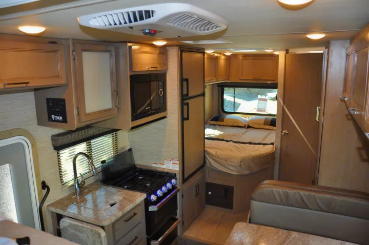 An RV rental interior showcasing a compact kitchen with stove/sink, a cozy bedroom, and dining area, ideal for travel.. Thor Daybreak 2021