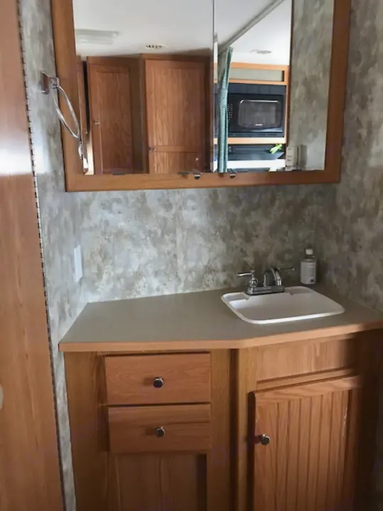 A mirrored wall reflects a microwave in this compact RV rental interior, featuring a small sink and wood cabinetry.. Winnebago Access 2007