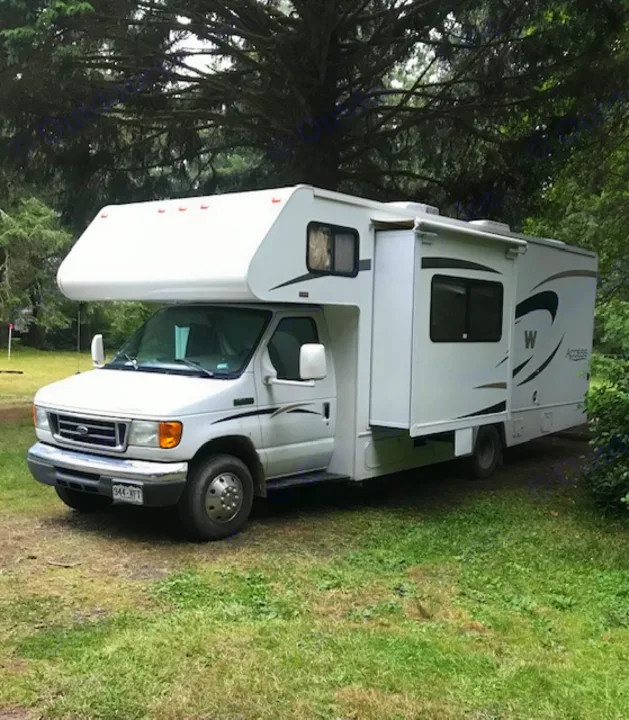 This white Class C RV, ideal for an RV rental, is parked on grass with trees in the background, ready for your next adventure.. Winnebago Access 2007