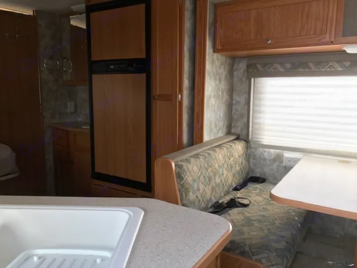RV rental: Kitchen sink, refrigerator, and booth dinette with patterned cushions by a window, ready for travel.. Winnebago Access 2007