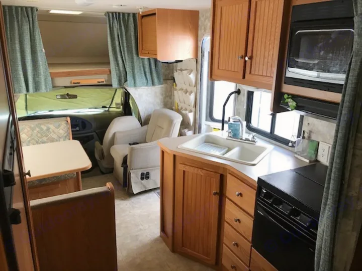 Inside this RV rental: a well-appointed kitchen, dining area, driver's cab, and cozy bunk bed above.. Winnebago Access 2007