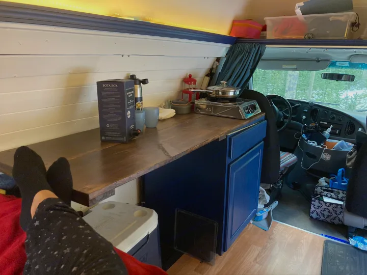 Cozy RV rental interior with a compact kitchen, lounge area, and window views. Perfect for van life.. Ford E350 Box Van 1997