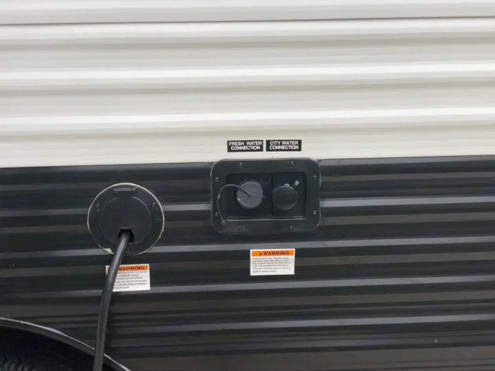 RV rental side panel: electrical power cord plugged in, and fresh/city water connections. Essential RV hookups for camping.. Keystone RV Hideout 2021