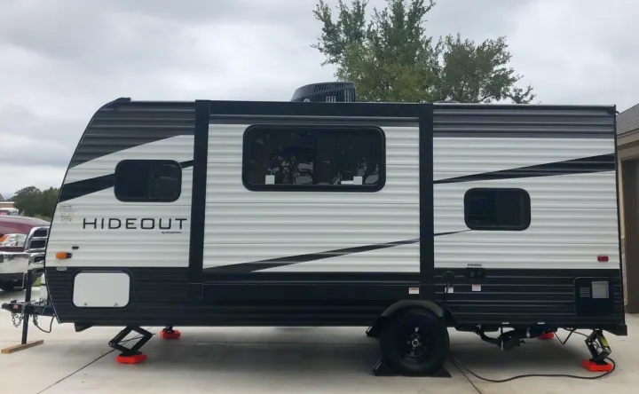 A black and white Hideout travel trailer, parked and stabilized on orange pads, ready as an rv rental.. Keystone RV Hideout 2021