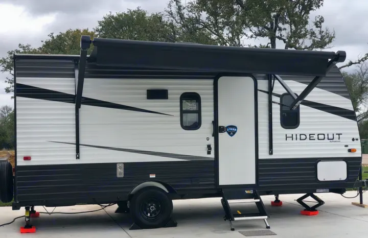 A parked black and white Keystone Hideout RV rental with its awning extended at a campsite, ready for adventure.. Keystone RV Hideout 2021