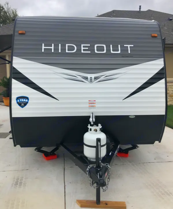 Front view of a modern Hideout travel trailer, perfect for an RV rental adventure. Grey, white, and black design with propane tank.. Keystone RV Hideout 2021