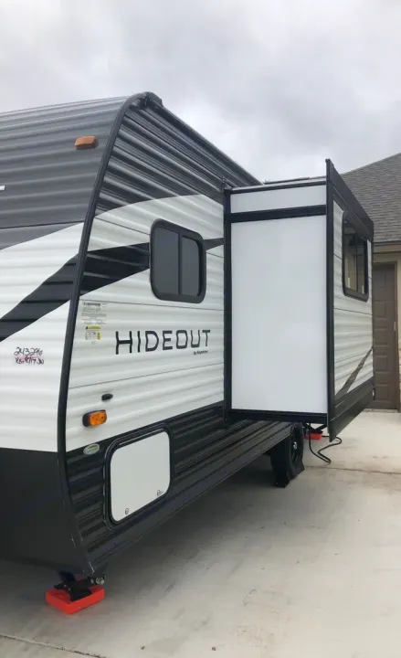 This RV rental, a black and white Hideout travel trailer, features an extended white slide-out on concrete.. Keystone RV Hideout 2021