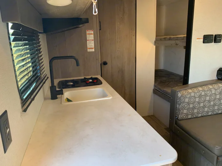 Inside this RV rental: a compact kitchen with stove & sink, plus comfy bunk beds and seating for your travel adventure.. Keystone Springdale 2021