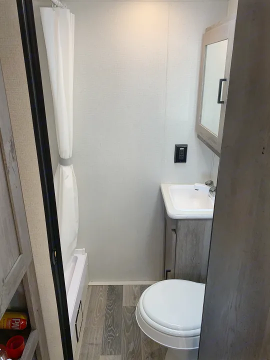Inside an RV rental: a bright, compact bathroom featuring a toilet, sink, and shower with curtain.. Keystone Springdale 2021