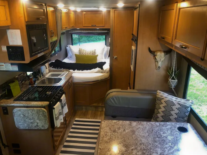 Inside a modern RV rental: a compact kitchen, dining area, and rear bedroom with cozy bedding, ready for adventure.. Other Four Winds 2018