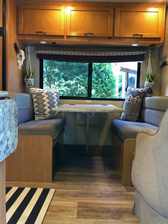 Cozy RV rental dinette with seating, a table, and windows overlooking nature, perfect for a comfortable travel experience.. Other Four Winds 2018