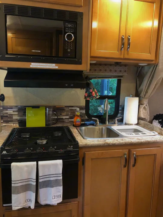 Inside an RV rental, this full kitchen has a Greystone microwave, gas stove, and double sink. Ready for cooking on the go.. Other Four Winds 2018