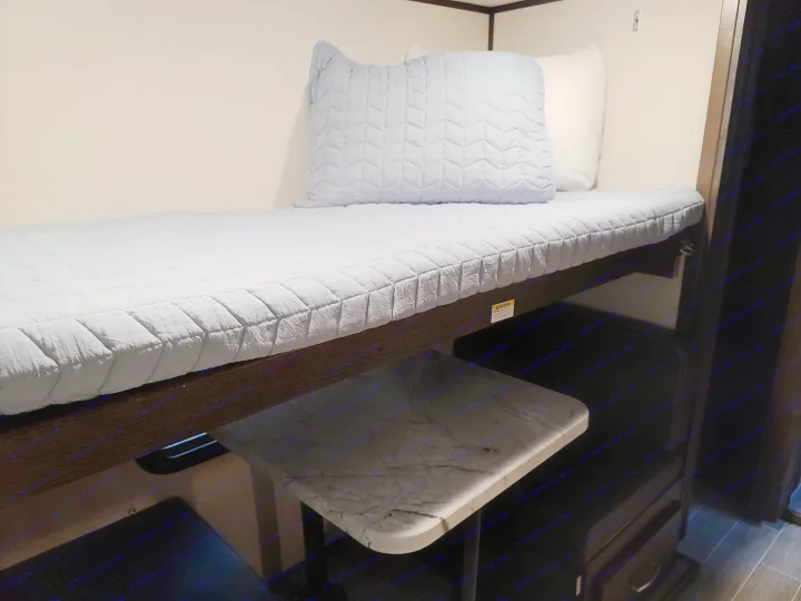 Discover this efficient RV rental bunk bed space, featuring quilted blue bedding, a pillow, and a handy lower table.. Dutchmen Other 2020