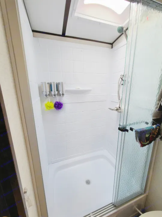 Inside a compact RV rental shower, featuring a wall dispenser, colorful loofahs, and a clear glass door.. Dutchmen Other 2020