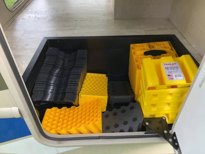 Open RV rental compartment showing neatly stacked black and yellow leveling blocks and wheel chocks for stability.. Thor Motor Coach Vegas 2020