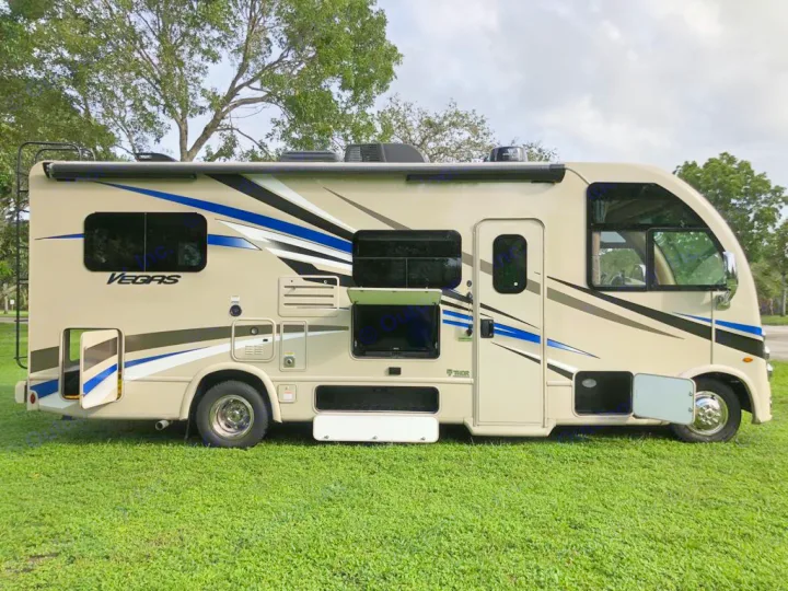 A beige Thor Vegas RV, sporting blue/black stripes, parked on green grass. This RV rental is ready for your next trip.. Thor Motor Coach Vegas 2020