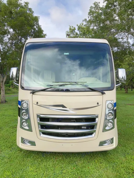 Full front view of a modern, cream-colored Class A motorhome parked on grass, perfect for your next rv rental adventure.. Thor Motor Coach Vegas 2020