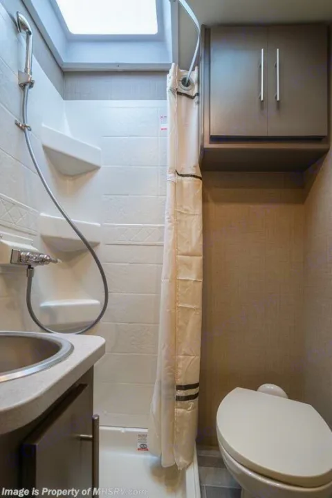 This RV rental bathroom features a compact shower, toilet, sink, and overhead cabinet, designed for travel comfort.. Thor Motor Coach Vegas 2020