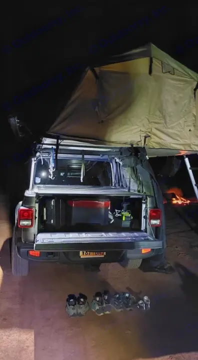 Nighttime overlanding setup: Jeep Gladiator with rooftop tent deployed. Gear in truck bed, shoes on ground. Great for RV rental adventures.. Jeep Gladiator 2020