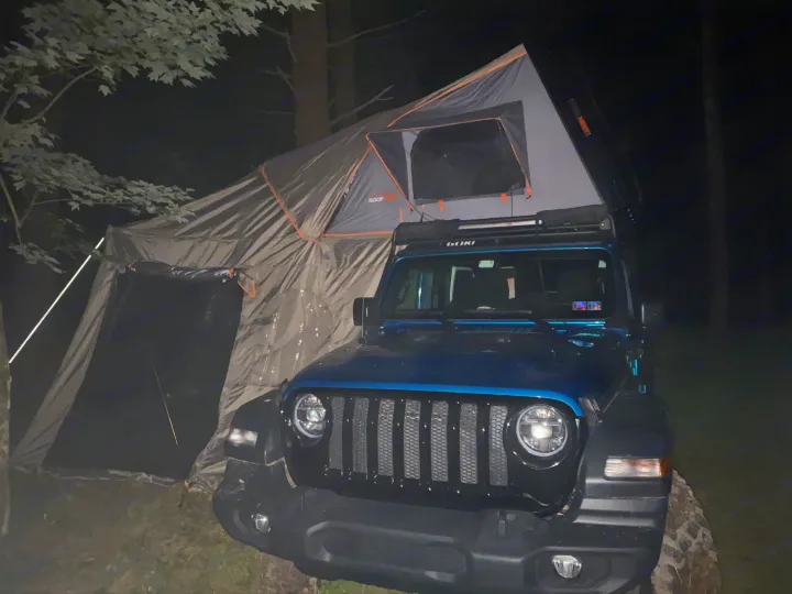 Nighttime: A dark blue Jeep with an extended rooftop tent and ground annex, resembling an rv rental setup.. Other Other 2020