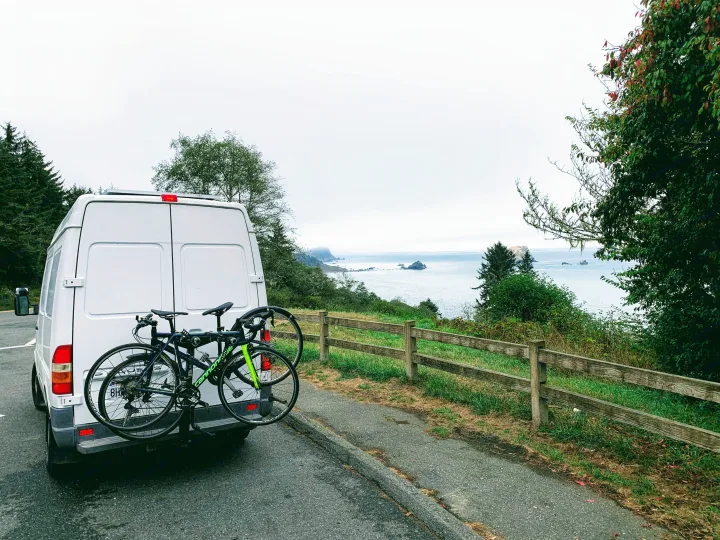 Enjoying a coastal road trip in an RV rental: white camper van with bikes parked overlooking the ocean and rocky coastline.. Mercedes Sprinter 2006