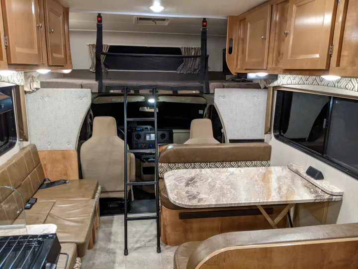 Interior of an rv rental with a fully equipped living area, dinettes, kitchen, and an over-cab bunk for sleeping.. Leprechaun 230RB 2020