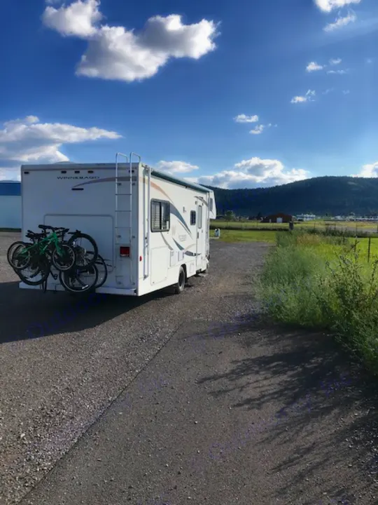 A white Winnebago RV rental, with bikes mounted on the back, parked on a paved lot overlooking mountains and sky.. Winnebago Access 2007