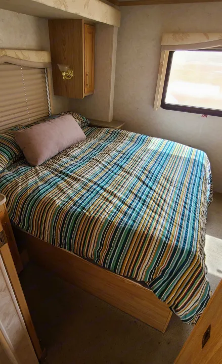 Cozy RV rental bedroom featuring a colorful striped bedspread, small window with 'EXIT' sign, and wood cabinets. Perfect for travel.. Fleetwood Bounder 2002