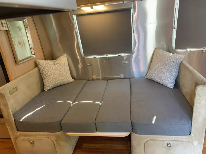 Inside an rv rental: inviting dinette converts to a bed, with comfortable grey cushions, tan benches, and shiny aluminum walls.. Airstream Safari 2006