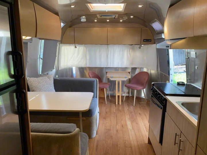Bright Airstream RV rental interior featuring a cozy dining booth, small lounge with two chairs, and compact kitchen with stove/sink.. Airstream Safari 2006