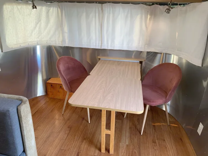 This RV rental offers a charming dining area with a modern wood table, pink velvet chairs, and metallic walls.. Airstream Safari 2006