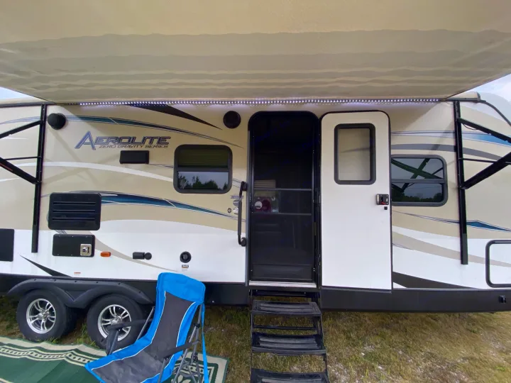 Side view of an Aerolite RV rental setup with extended awning, bright lights, and entry steps. Ready for outdoor camping.. Dutchmen Aerolite 2017