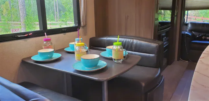 RV rental travel: Step inside this cozy RV dinette, set for four with bowls and straw jars, overlooking a peaceful outdoor scene.. Keystone RV Laredo 2020