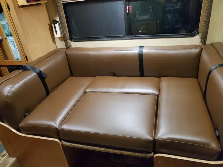An RV rental interior features a clean, brown faux leather dinette and sofa that can convert into a bed, by a window.. Thor Motor Coach Freedom Elite 2015