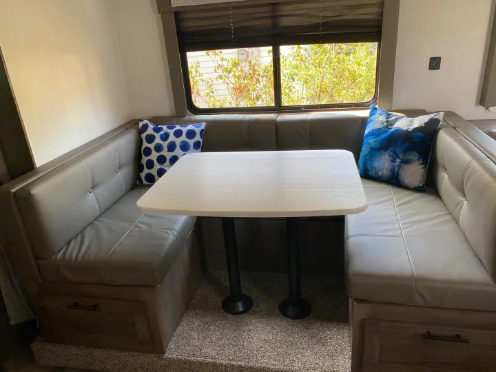 Cozy RV rental dinette: U-shaped gray bench seating, light table, pillows, and window views. Storage below.. Forest River Salem Cruise Lite 2021