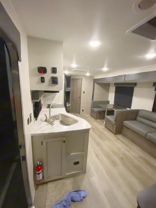 Bright rv rental interior showing a compact kitchen with sink, adjacent living area with sofa, and wood-look floor.. Open Range Open Range 2021