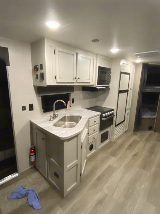 RV rental: Well-appointed kitchen with white cabinets, sink, stove, microwave, and light wood flooring.. Open Range Open Range 2021