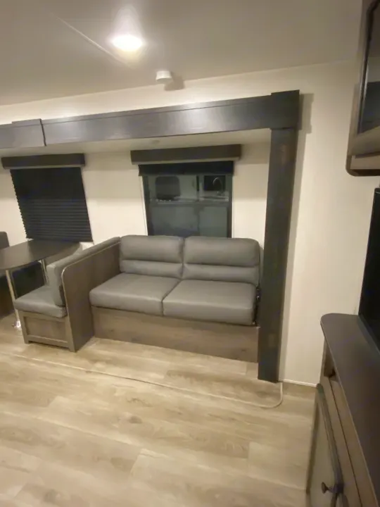 RV rental interior: Cozy living space with a grey sofa, window, and light wood flooring.. Open Range Open Range 2021