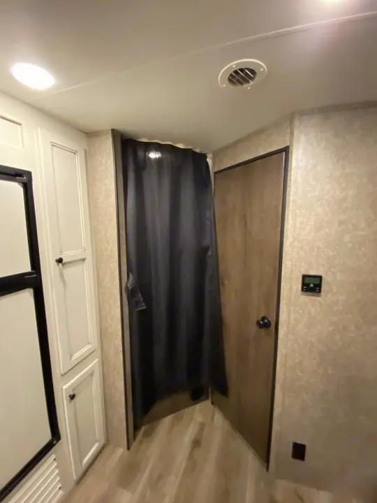 Inside an RV rental: a cozy bunk bed with a dark privacy curtain, overhead cabinets, and a vent.. Open Range Open Range 2021