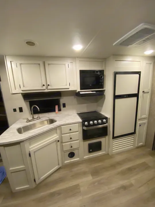 Modern RV rental kitchen featuring light cabinets, corner sink, microwave, stove, and refrigerator for comfortable living.. Open Range Open Range 2021