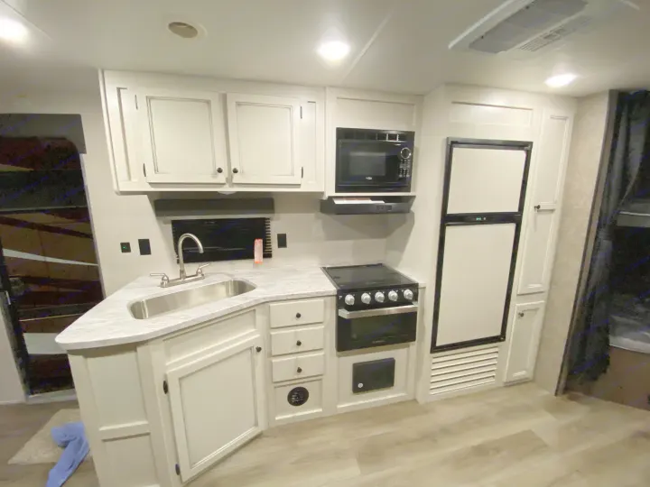 Modern RV rental kitchen featuring white cabinets, stainless steel sink, microwave, stove, and refrigerator.. Open Range Open Range 2021