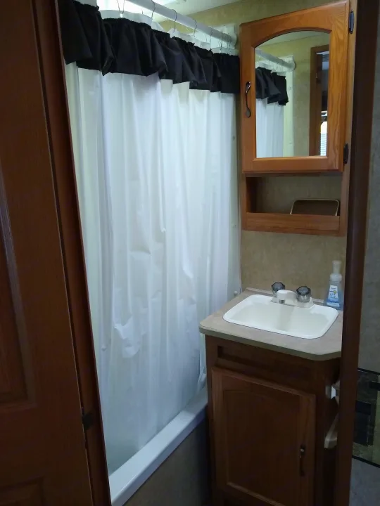 Compact RV rental bathroom: features a white shower curtain, sink vanity, and wooden medicine cabinet for your journey.. Frontier Hyperlite 28RBH 2008