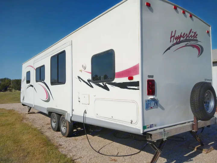 White Hyperlite travel trailer RV rental, equipped with leveling jacks, parked on gravel under a clear sky.. Frontier Hyperlite 28RBH 2008