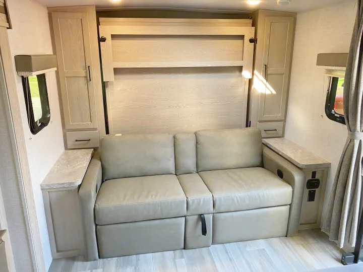 Spacious RV rental interior with a light grey sofa and built-in murphy bed, surrounded by light wood cabinetry. Perfect for travel.. Forest River Mini-Lite 2021