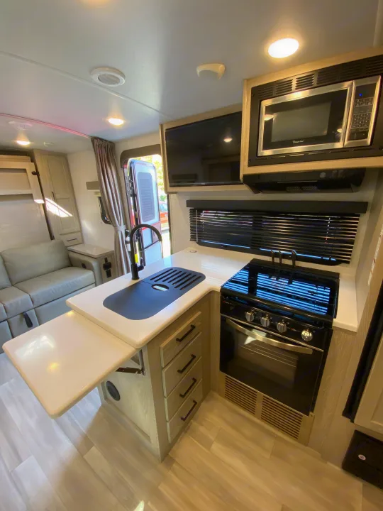 An RV rental's modern kitchen boasts a stove, microwave, sink, and TV, adjacent to a cozy living space with a sofa.. Forest River Mini-Lite 2021