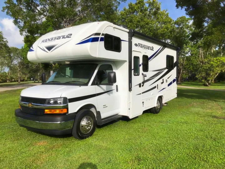 Explore the outdoors with this spacious white RV rental, featuring striking black and blue details, parked on green grass.. Forest River sunseeker LE 2350 2020