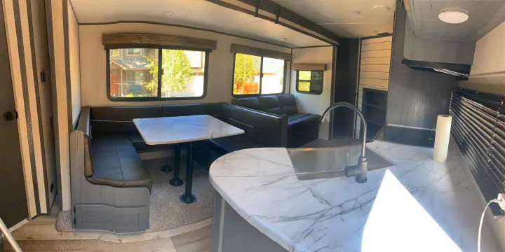 Modern RV rental interior: large dinette, comfortable sofa, and a well-lit kitchen with a marble-patterned counter and sink.. Dutchmen Aspen Trail 2021