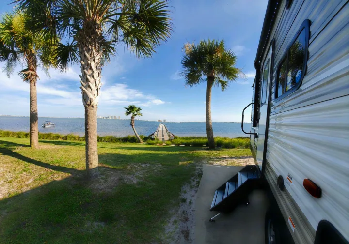 Relaxing RV rental view: waterfront campsite with palm trees, a pier, and a calm bay.. Dutchmen Aspen Trail 26BH 2021