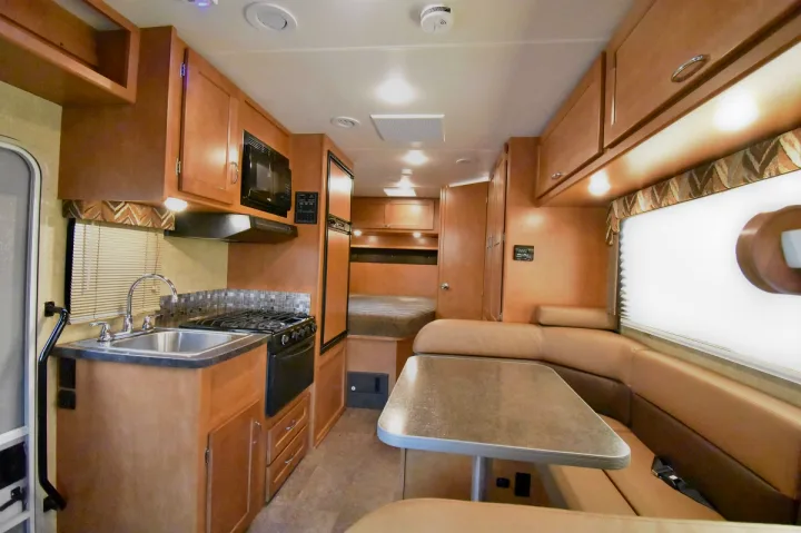 Step into this bright RV rental interior, featuring a compact kitchen, U-shaped dining area, and a bed. Functional and modern.. Winnebago Minnie Winnie 2019
