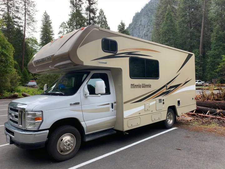 A white and tan Winnebago Minnie Winnie RV rental, perfect for a camping trip in a scenic mountain park.. Winnebago Minnie Winnie 2019